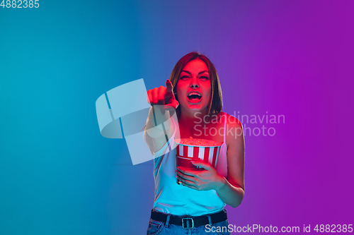 Image of Caucasian young woman\'s portrait isolated on gradient purple-blue background in neon light, cinema, movie watching