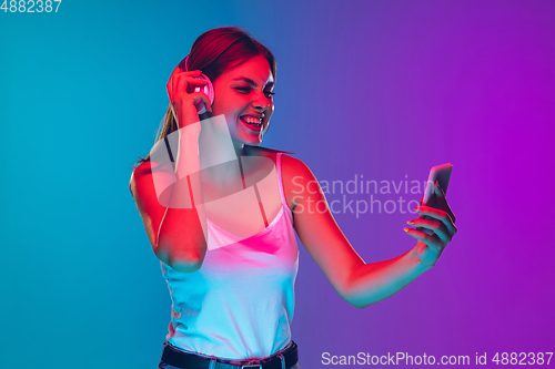 Image of Caucasian young woman\'s portrait isolated on gradient purple-blue background in neon light
