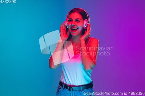 Image of Caucasian young woman\'s portrait isolated on gradient purple-blue background in neon light