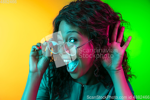 Image of African-american young woman\'s portrait isolated on gradient yellow-green background in neon light