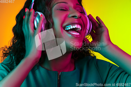 Image of African-american young woman\'s portrait isolated on gradient yellow-green background in neon light