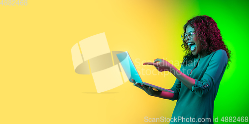 Image of African-american young woman\'s portrait isolated on gradient yellow-green background in neon light