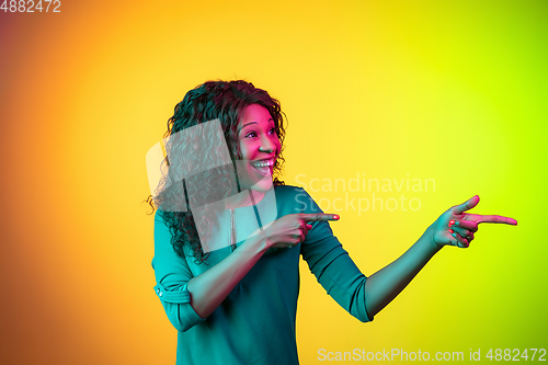 Image of African-american young woman\'s portrait isolated on gradient yellow-green background in neon light