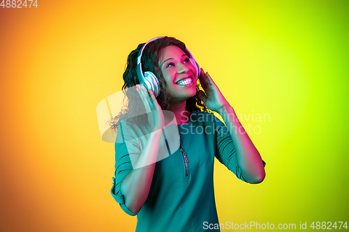 Image of African-american young woman\'s portrait isolated on gradient yellow-green background in neon light