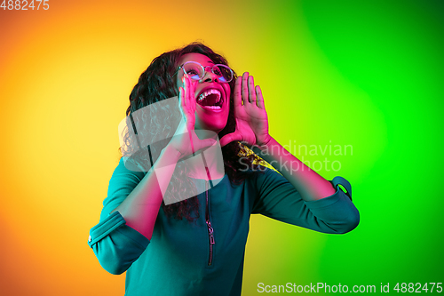 Image of African-american young woman\'s portrait isolated on gradient yellow-green background in neon light