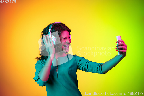 Image of African-american young woman\'s portrait isolated on gradient yellow-green background in neon light