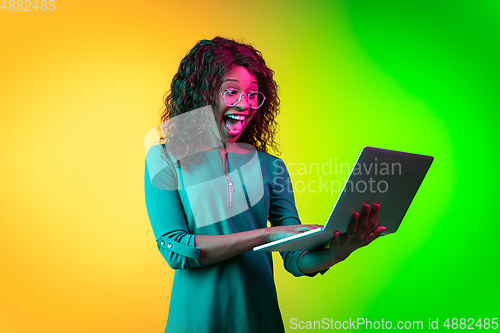 Image of African-american young woman\'s portrait isolated on gradient yellow-green background in neon light