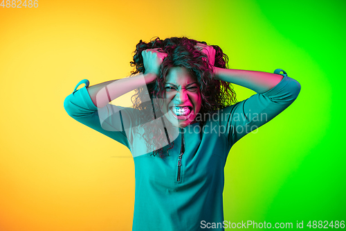 Image of African-american young woman\'s portrait isolated on gradient yellow-green background in neon light