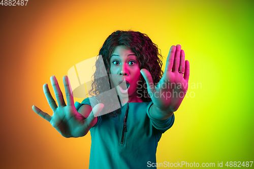 Image of African-american young woman\'s portrait isolated on gradient yellow-green background in neon light