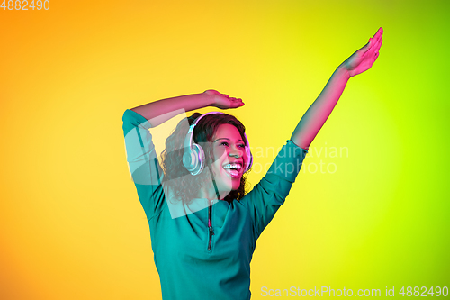 Image of African-american young woman\'s portrait isolated on gradient yellow-green background in neon light