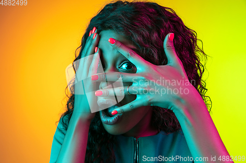 Image of African-american young woman\'s portrait isolated on gradient yellow-green background in neon light