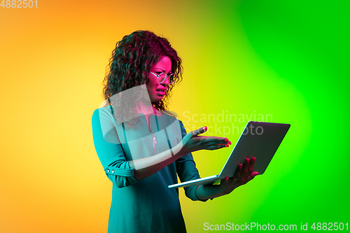 Image of African-american young woman\'s portrait isolated on gradient yellow-green background in neon light