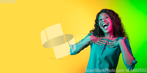 Image of African-american young woman\'s portrait isolated on gradient yellow-green background in neon light