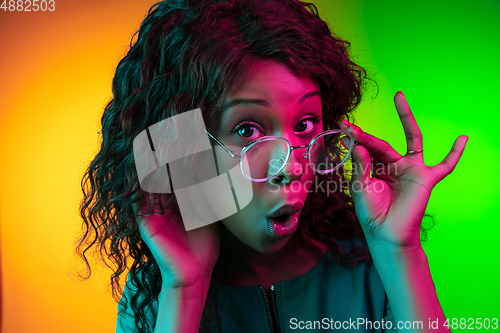 Image of African-american young woman\'s portrait isolated on gradient yellow-green background in neon light