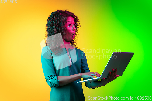 Image of African-american young woman\'s portrait isolated on gradient yellow-green background in neon light