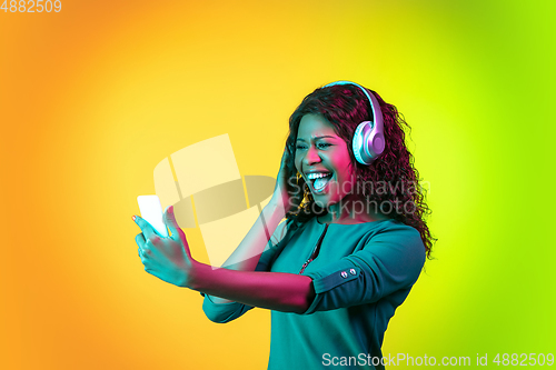 Image of African-american young woman\'s portrait isolated on gradient yellow-green background in neon light