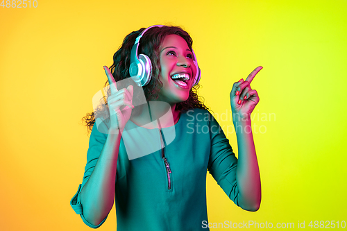 Image of African-american young woman\'s portrait isolated on gradient yellow-green background in neon light