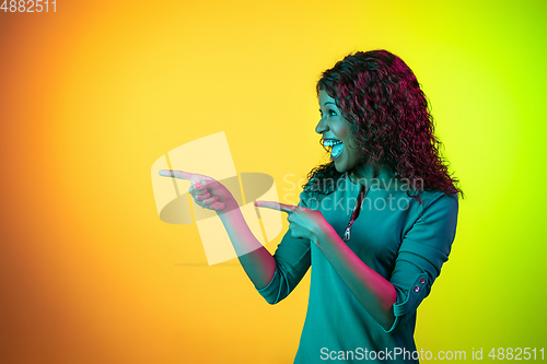 Image of African-american young woman\'s portrait isolated on gradient yellow-green background in neon light
