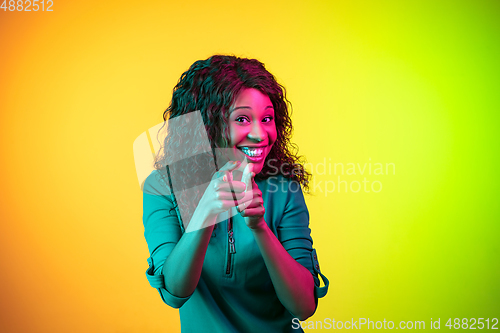 Image of African-american young woman\'s portrait isolated on gradient yellow-green background in neon light