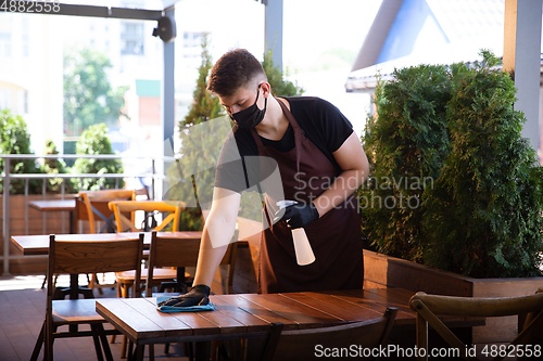 Image of The waiter works in a restaurant in a medical mask, gloves during coronavirus pandemic