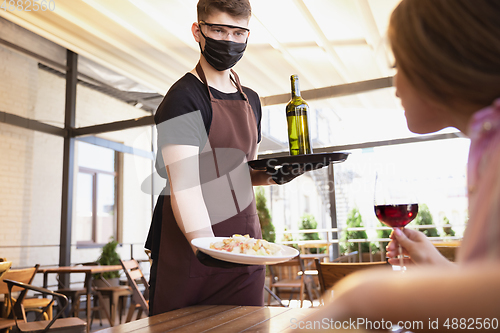 Image of The waiter works in a restaurant in a medical mask, gloves during coronavirus pandemic