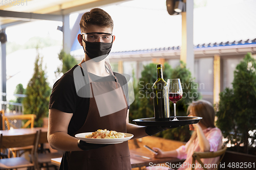 Image of The waiter works in a restaurant in a medical mask, gloves during coronavirus pandemic