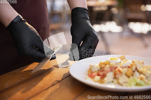 Image of The waiter works in a restaurant in a medical mask, gloves during coronavirus pandemic