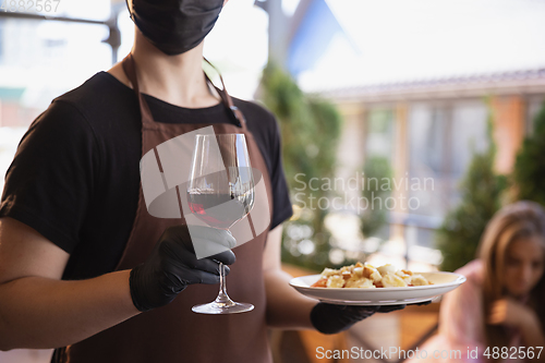 Image of The waiter works in a restaurant in a medical mask, gloves during coronavirus pandemic