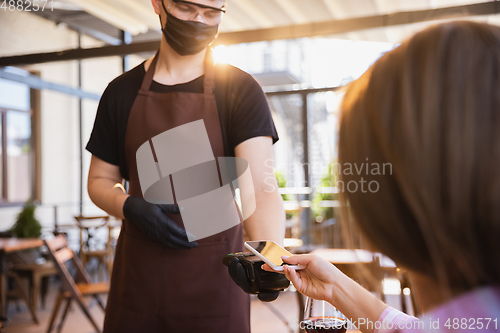 Image of The waiter works in a restaurant in a medical mask, gloves during coronavirus pandemic