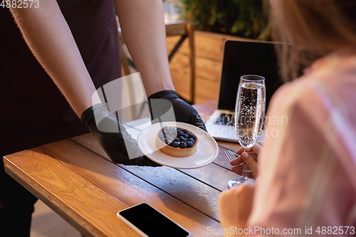 Image of The waiter works in a restaurant in a medical mask, gloves during coronavirus pandemic