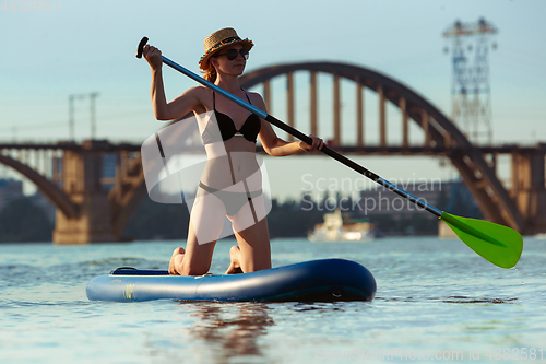 Image of Young attractive woman sitting on paddle board, SUP. Active life, sport, leisure activity concept