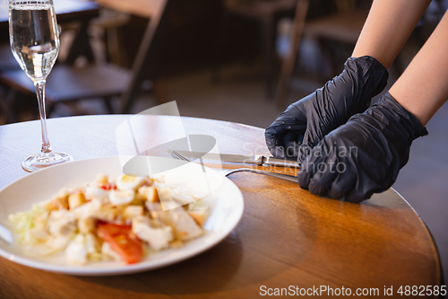 Image of The waitress works in a restaurant in a medical mask, gloves during coronavirus pandemic