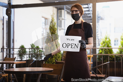 Image of The waitress works in a restaurant in a medical mask, gloves during coronavirus pandemic