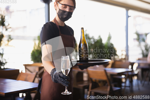 Image of The waitress works in a restaurant in a medical mask, gloves during coronavirus pandemic