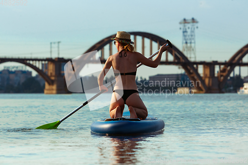 Image of Young attractive woman sitting on paddle board, SUP. Active life, sport, leisure activity concept