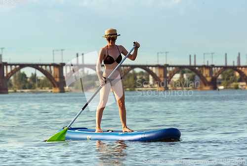 Image of Young attractive woman standing on paddle board, SUP. Active life, sport, leisure activity concept