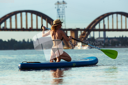 Image of Young attractive woman sitting on paddle board, SUP. Active life, sport, leisure activity concept