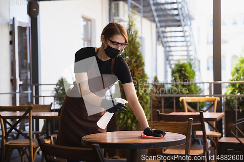 Image of The waitress works in a restaurant in a medical mask, gloves during coronavirus pandemic