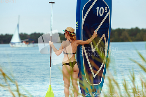 Image of Young attractive woman standing next to paddle board, SUP. Active life, sport, leisure activity concept