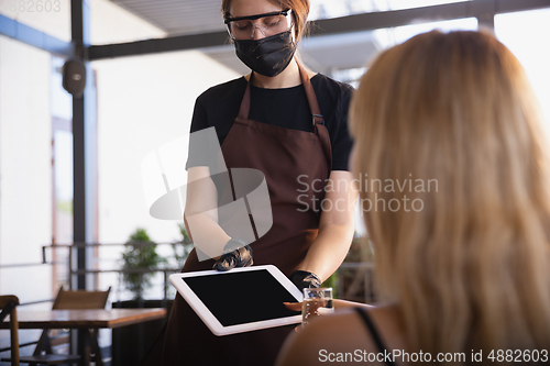 Image of The waitress works in a restaurant in a medical mask, gloves during coronavirus pandemic