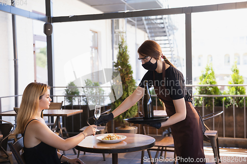 Image of The waitress works in a restaurant in a medical mask, gloves during coronavirus pandemic