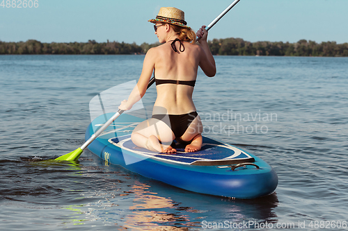 Image of Young attractive woman sitting on paddle board, SUP. Active life, sport, leisure activity concept