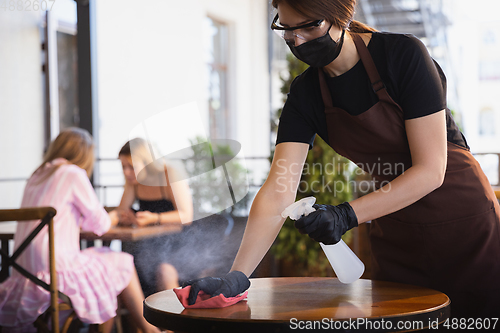 Image of The waitress works in a restaurant in a medical mask, gloves during coronavirus pandemic