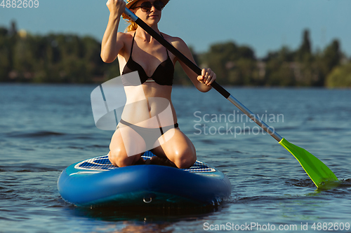 Image of Young attractive woman sitting on paddle board, SUP. Active life, sport, leisure activity concept