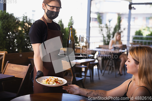 Image of The waitress works in a restaurant in a medical mask, gloves during coronavirus pandemic