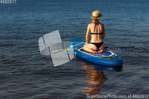 Image of Young attractive woman sitting on paddle board, SUP. Active life, sport, leisure activity concept