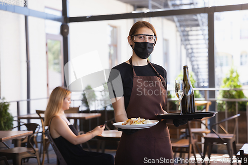 Image of The waitress works in a restaurant in a medical mask, gloves during coronavirus pandemic