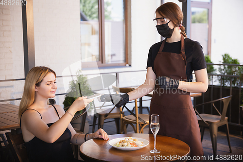 Image of The waitress works in a restaurant in a medical mask, gloves during coronavirus pandemic