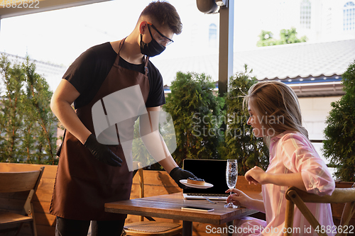 Image of The waiter works in a restaurant in a medical mask, gloves during coronavirus pandemic