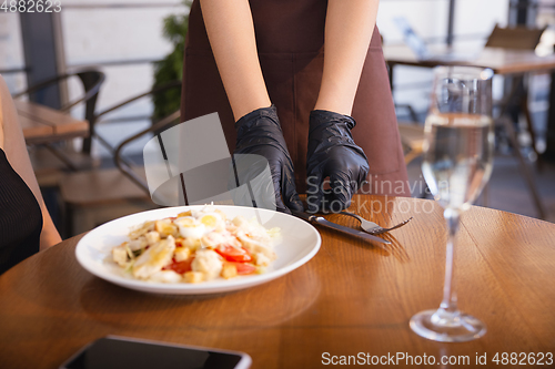 Image of The waitress works in a restaurant in a medical mask, gloves during coronavirus pandemic